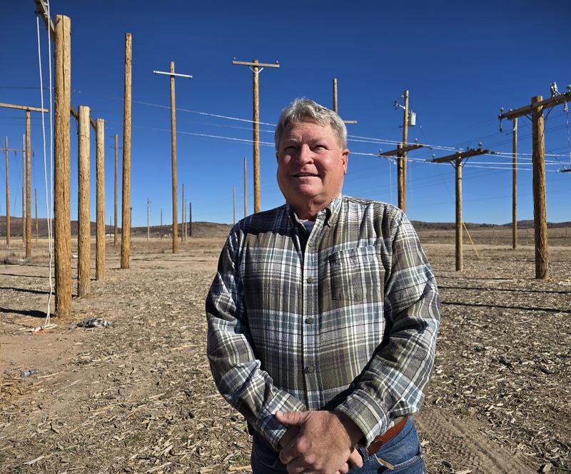 Picture of a man in a plaid shirt standing in front of a field of electrical line posts used for training