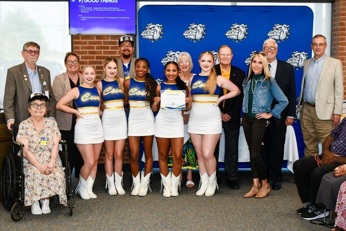 A group of dancers in uniform with their coach and school board members, holding an award.
