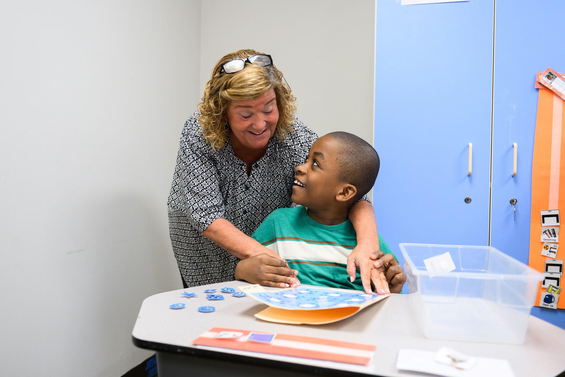 Teacher leaning over student who is sitting and showing lesson.