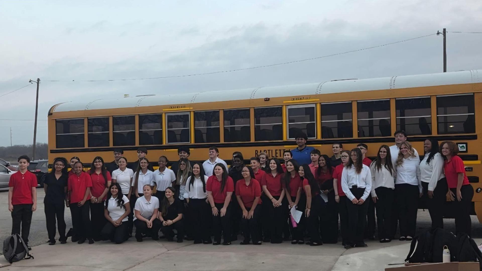 Large group of students in red and white shirts gathered by a school bus.