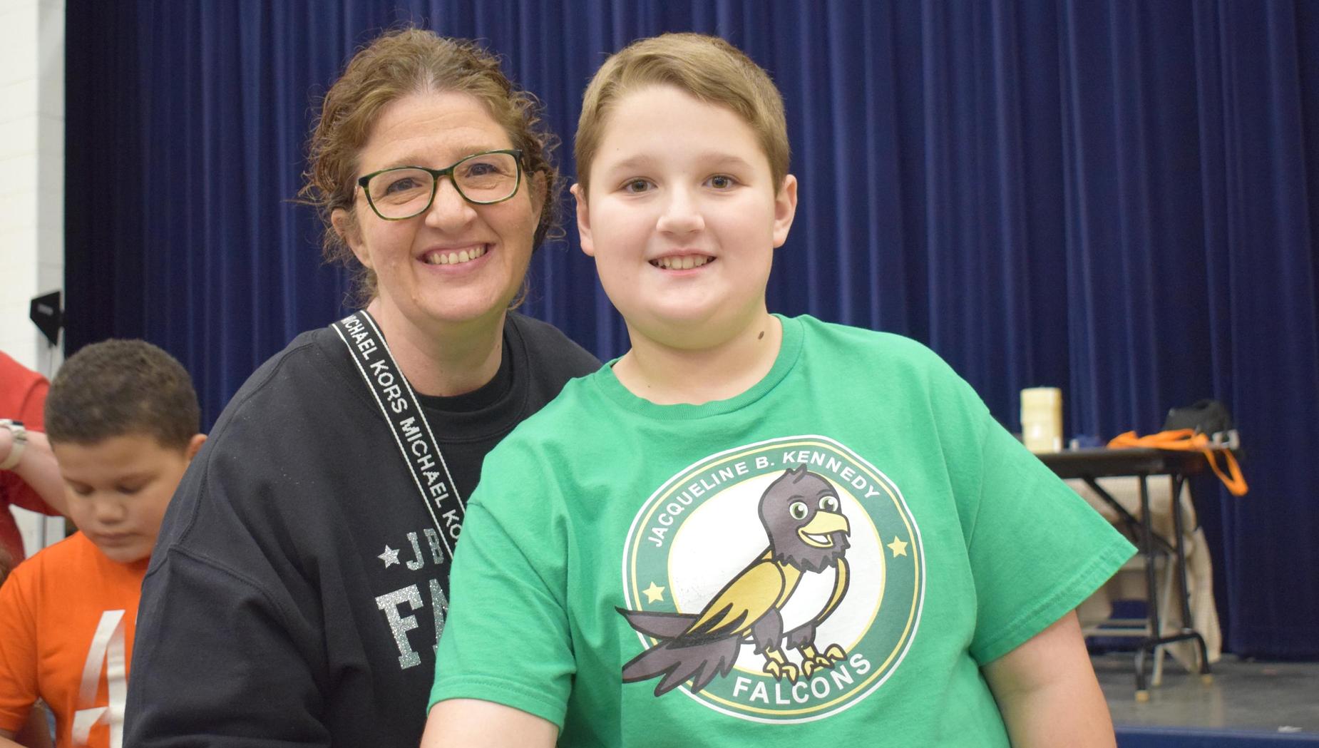 A woman and a boy with a falcon logo shirt smiling at the camera.