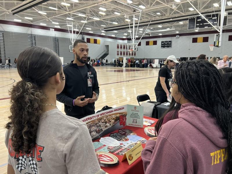 Two students engage with a representative at a college fair booth.