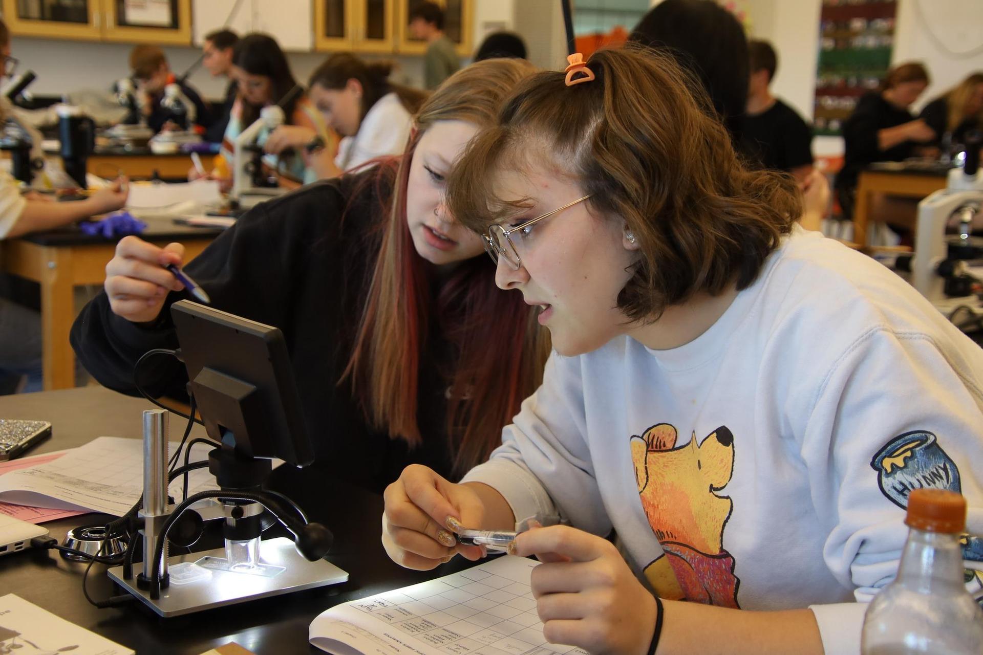 two high school students working looking through a microscope in a science classroom