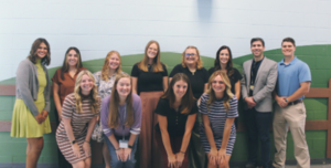 12 new hires smile at camera in front of fenced wall