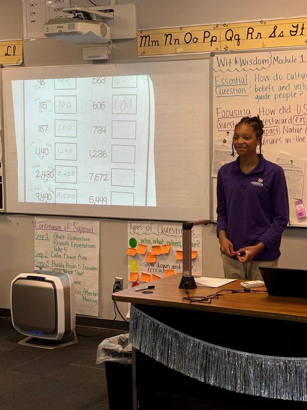 A scholar stands at the front of the class teaching a math lesson