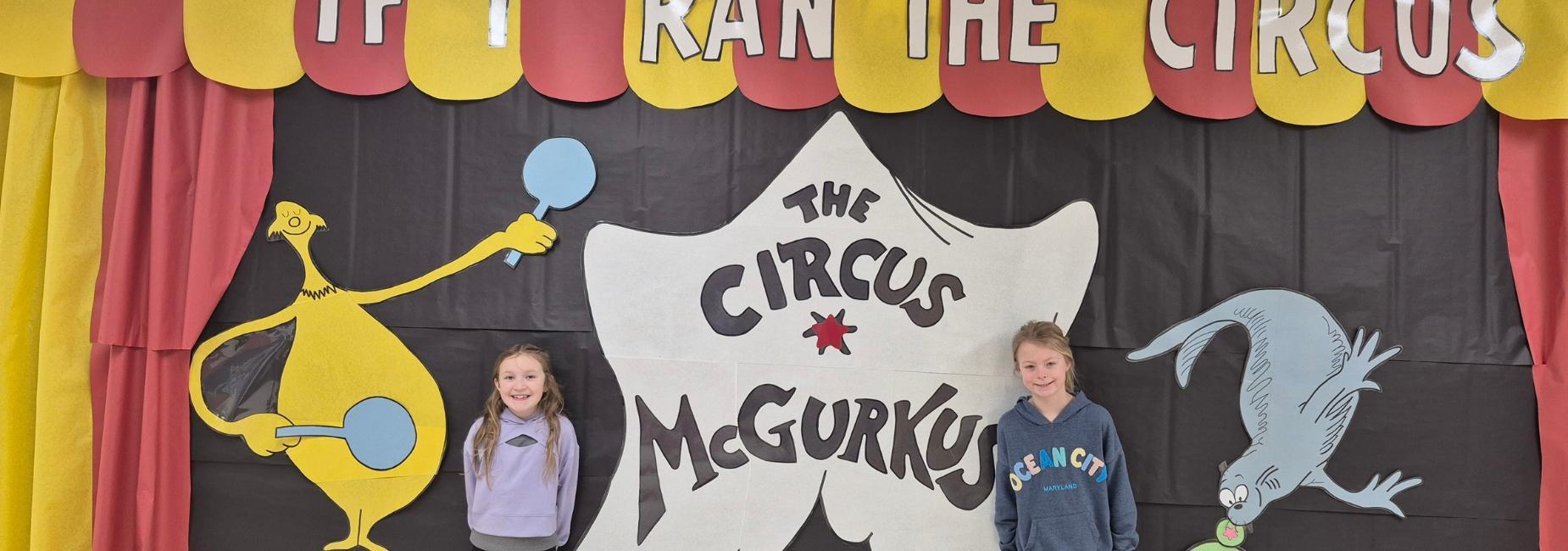 Two children posing under a circus-themed banner with whimsical characters.