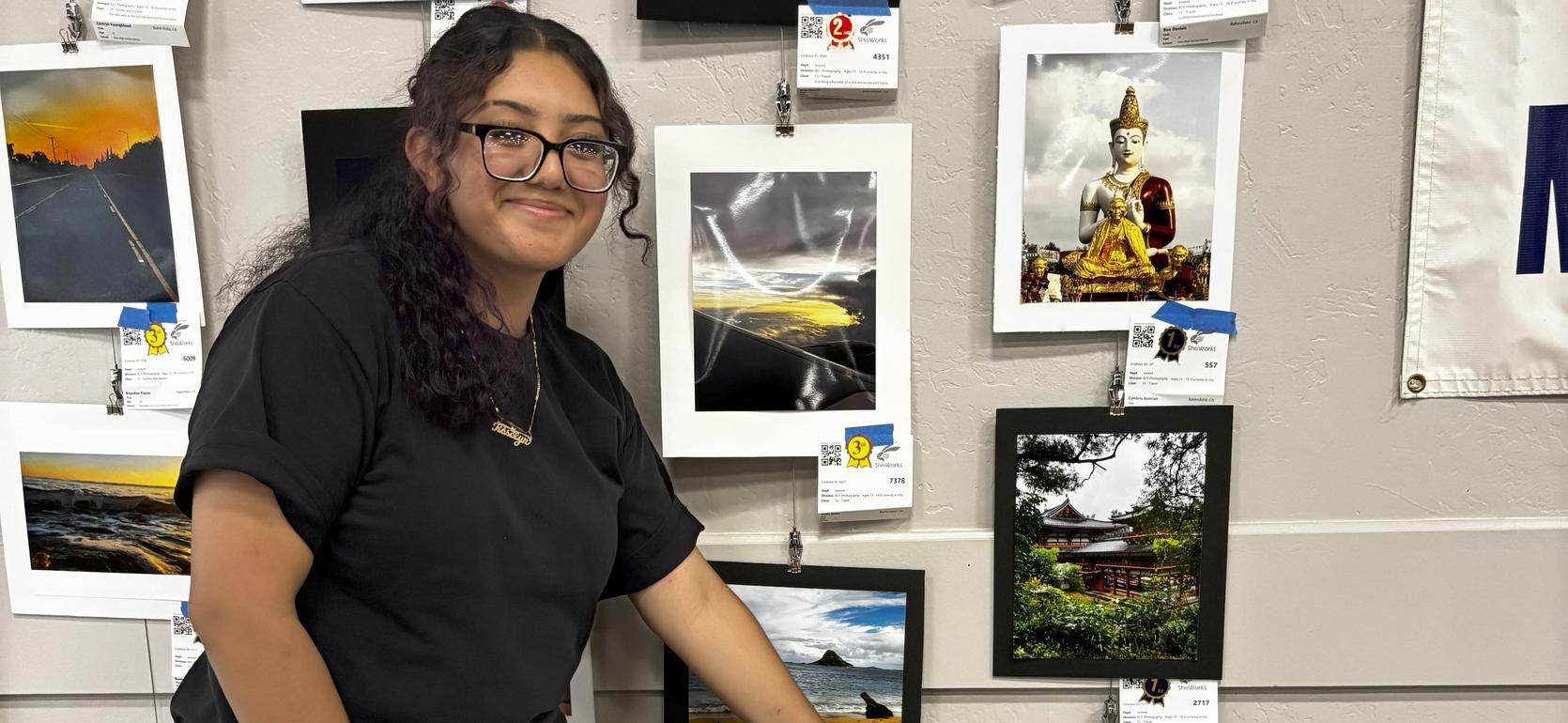 A person pointing at a black and white photograph among several framed artworks on a wall.