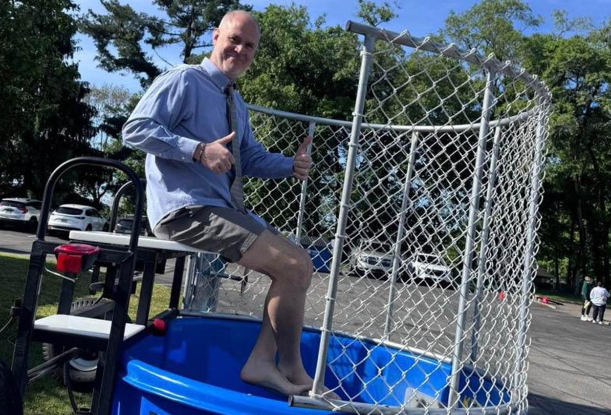 Mr. DiNapoli sits in a dunking booth with two thumbs up