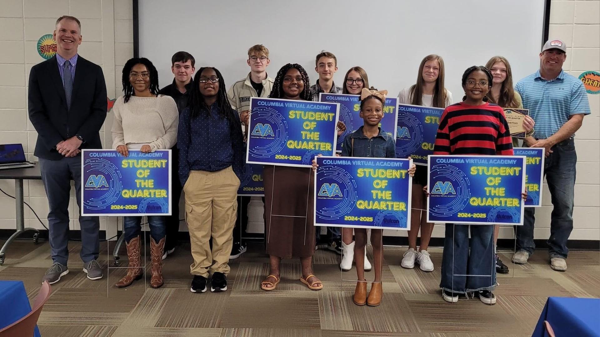 Group of students holding 'Student of the Quarter' signs with teachers at a ceremony.