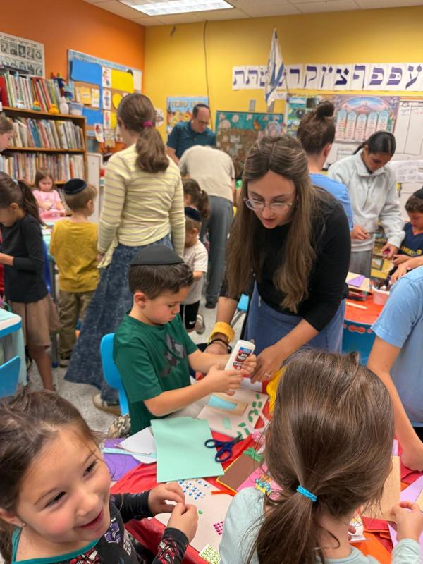 A kindergarten boy enjoys making a sukkah decoration with his mother.
