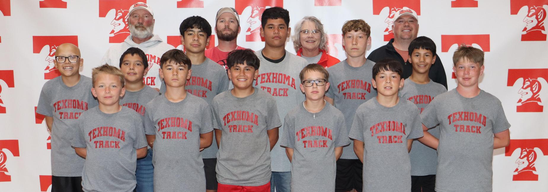 Boys in gray shirts posing for a team photo, with adults in the background.