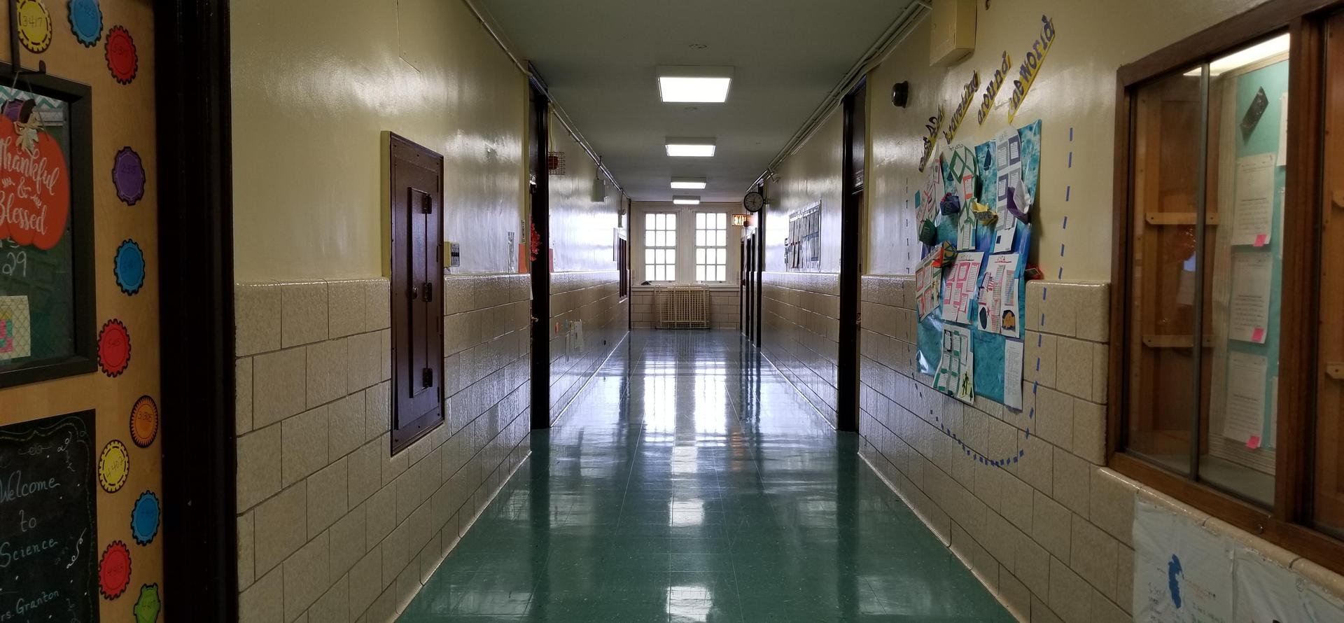 Empty school hallway with green flooring and bulletin boards.