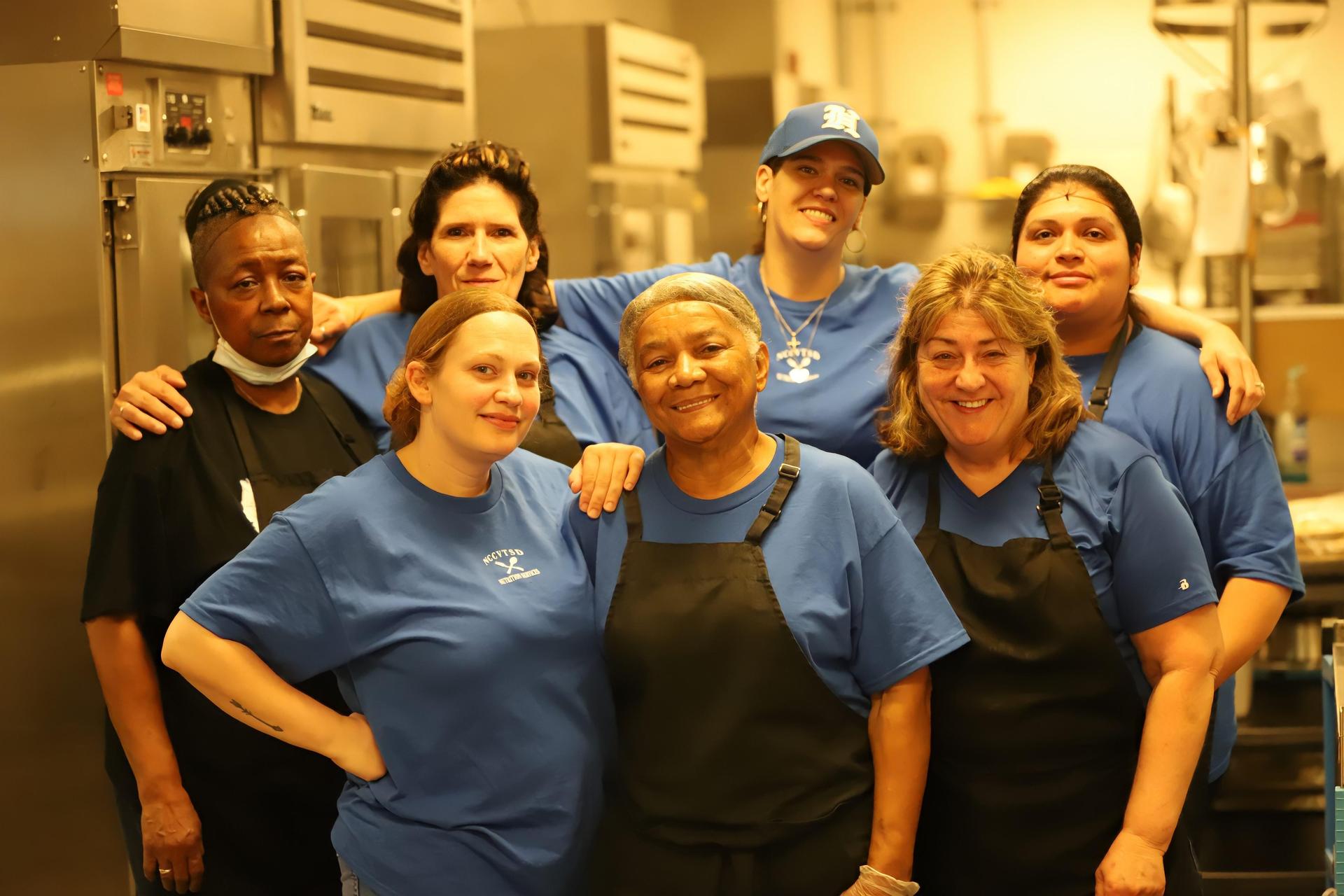Cheerful group of seven food service workers in blue shirts posing together.