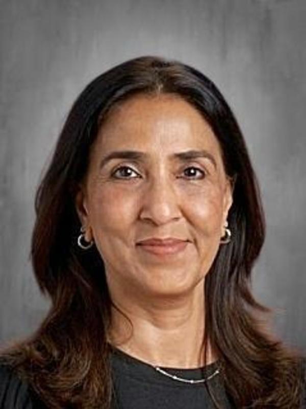 A smiling woman with long dark hair and earrings against a gray background.