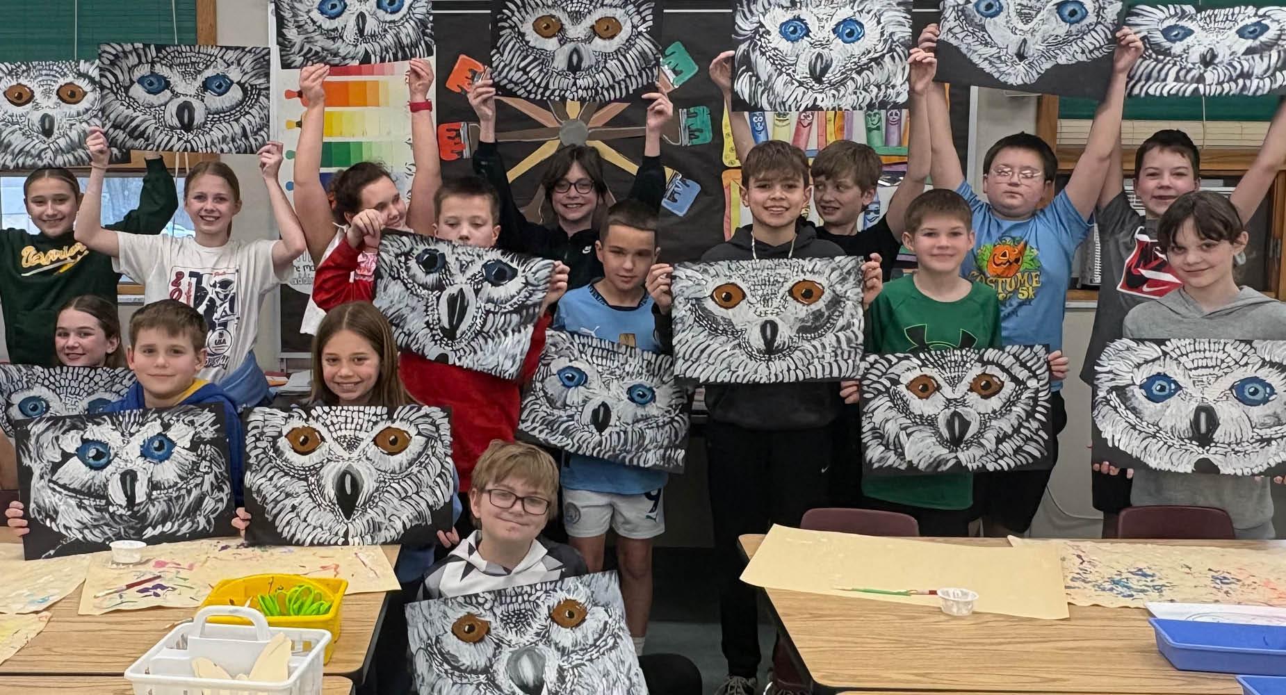 Students hold up their paintings of owls that they completed in art class