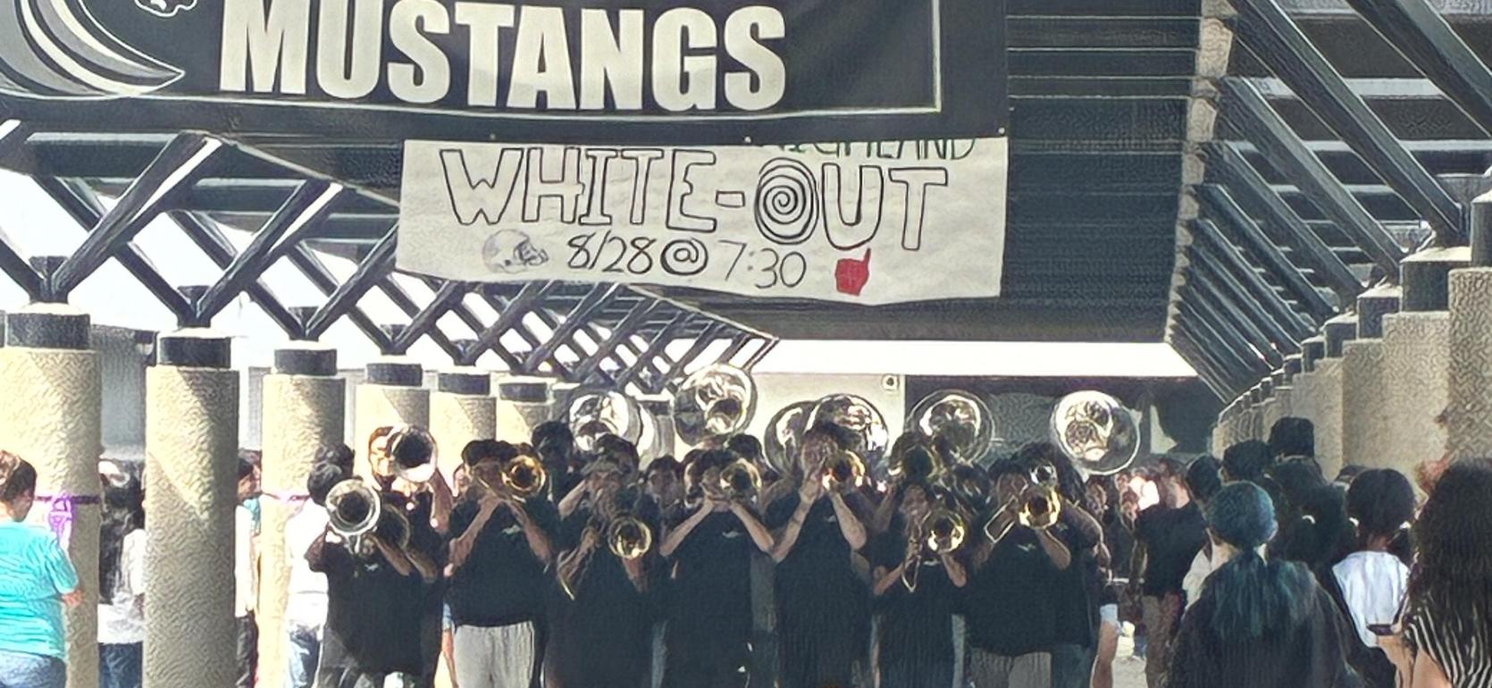 A marching band performing under a banner in a crowded area.