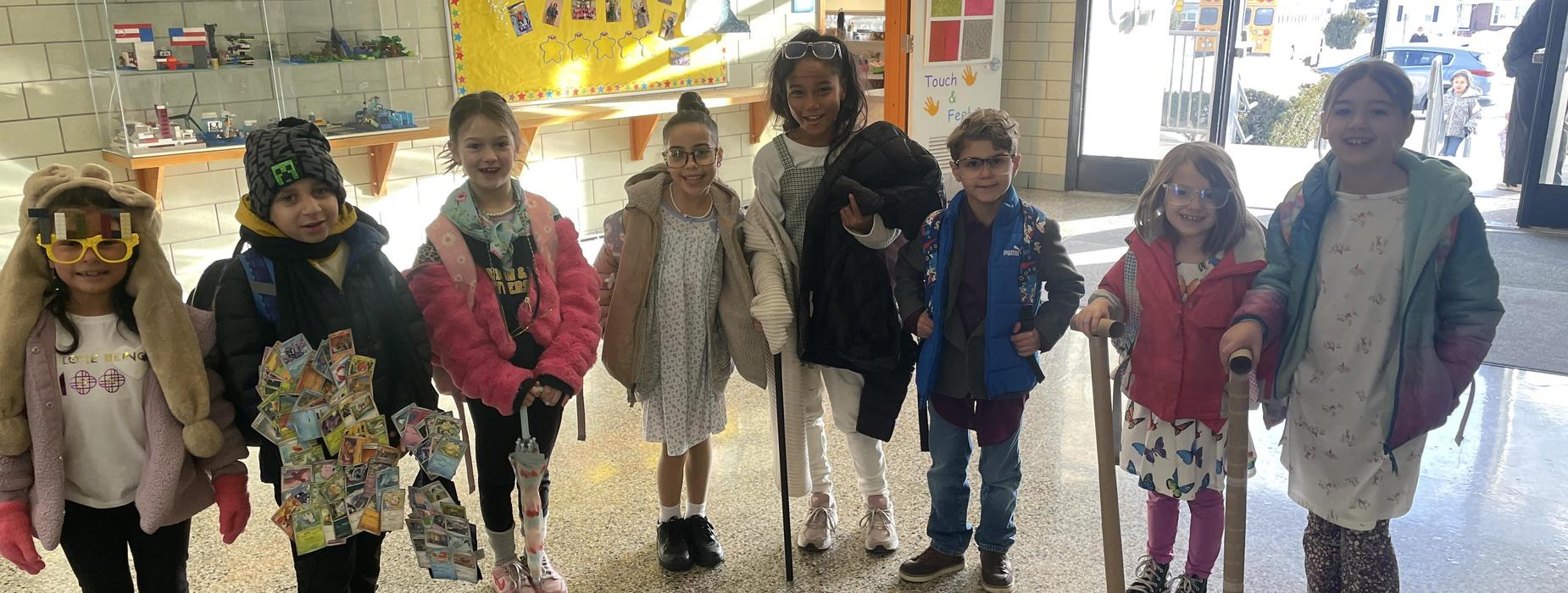 Eight students pose together in the lobby of a school dressed in vintage clothing for the 100th day of school.