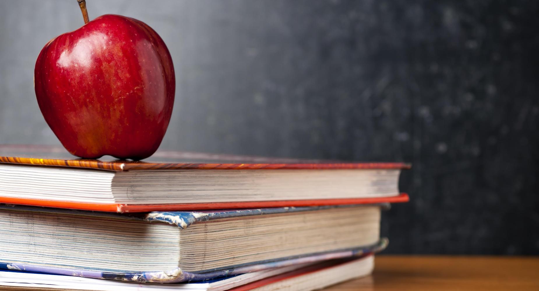 A red apple sits atop a stack of books against a dark background.