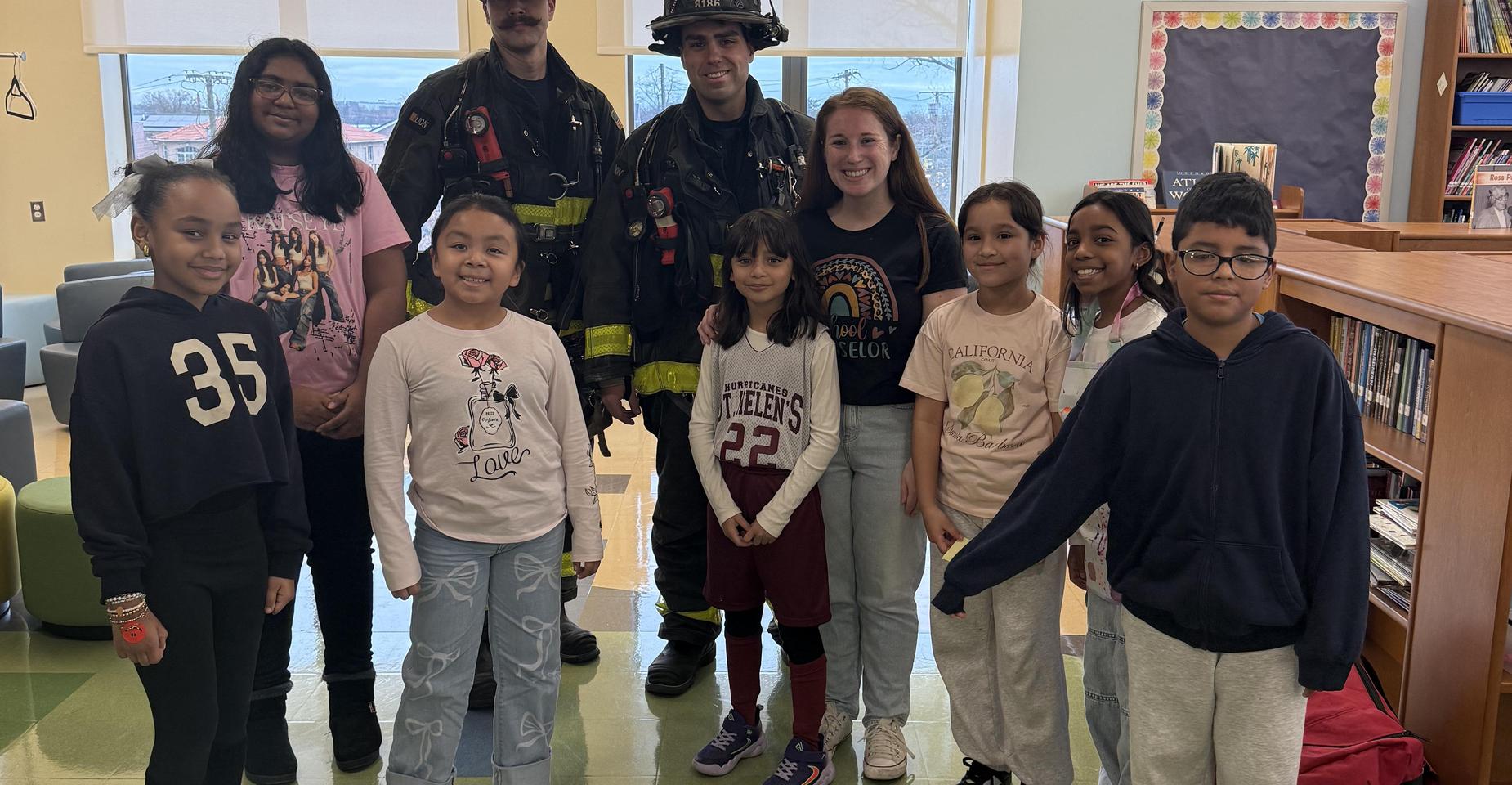 A group of children and two firefighters posing together in a library setting.
