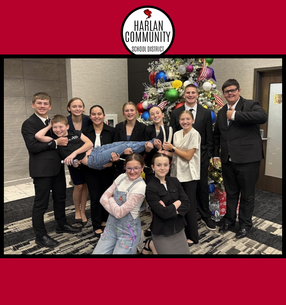 Group of students in formal attire posing playfully in front of a decorated tree.
