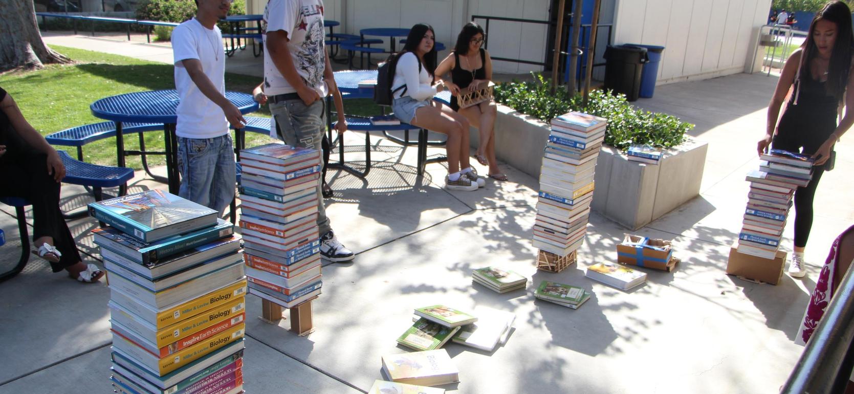 Several stacks of colorful books arranged around a courtyard with people sitting nearby.