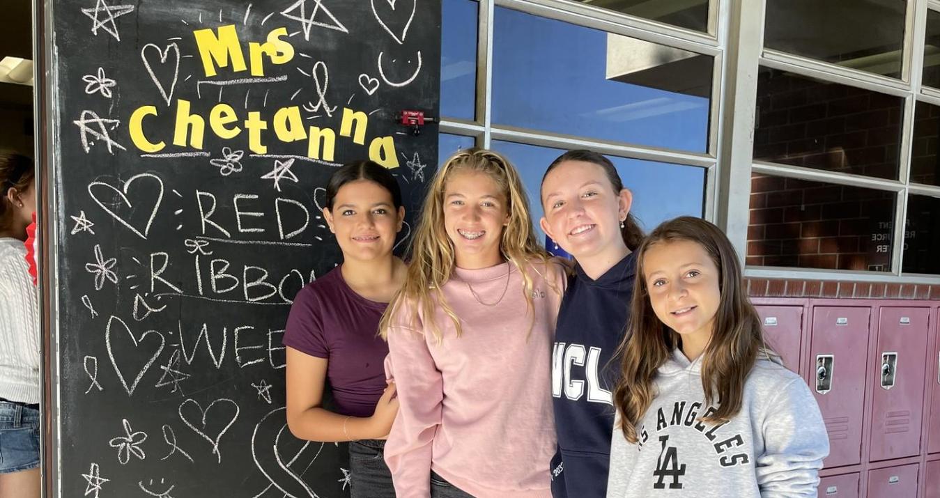 Four girls pose together in front of a chalkboard with decorative drawings.
