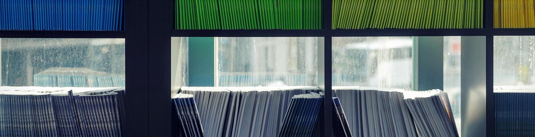Colorful folders arranged on shelves with sunlight filtering through windows.
