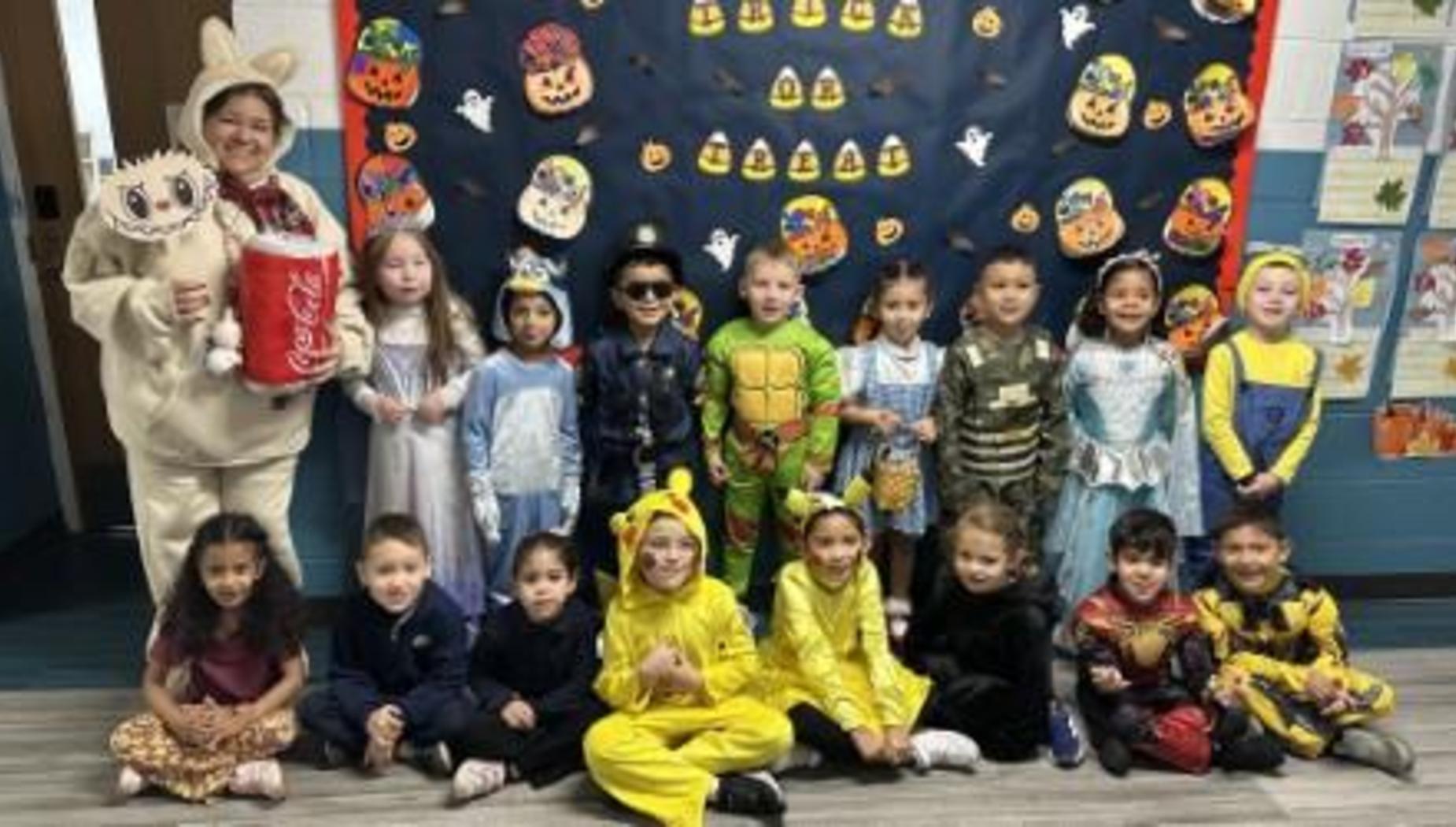 Group of children in costumes posing in front of a decorated wall for Halloween.