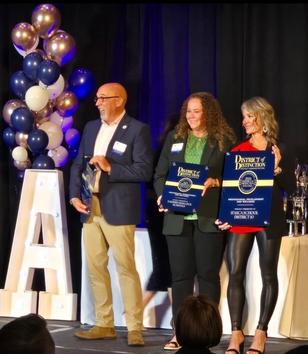Three individuals stand on stage holding awards at a formal event with balloons in the background.