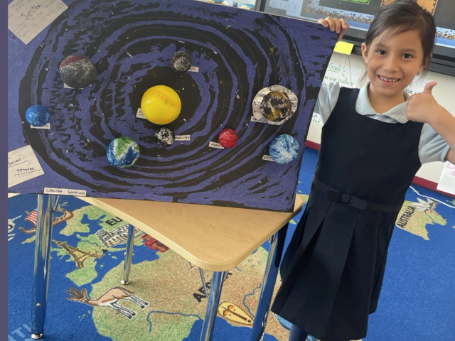 A girl stands by a solar system project with planets on display.