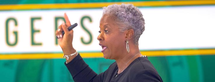 A woman with gray hair passionately speaks while gesturing with one hand.