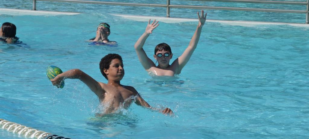 2 boys toss a football in the pool