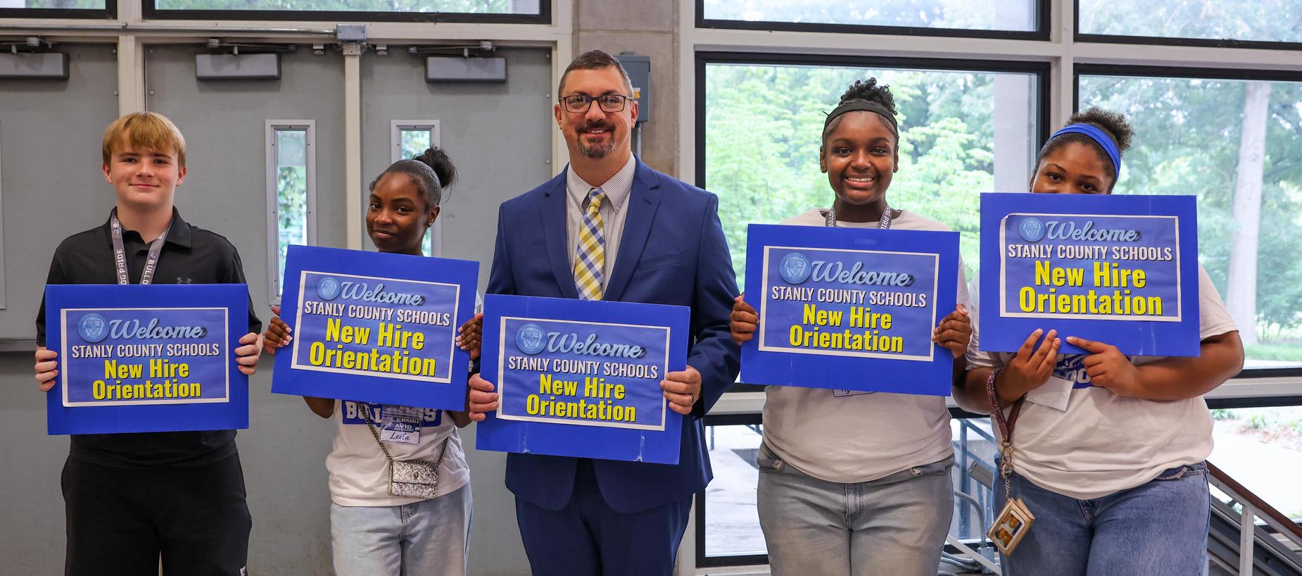 Group of new hires holding welcome signs at orientation event.