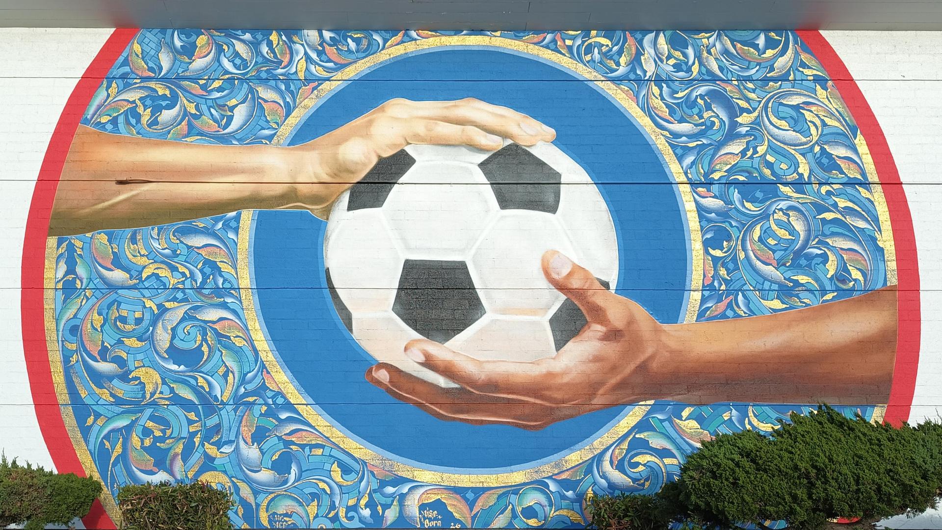 FIFA 2026 Mural of Soccer Ball with one hand on top and one on the bottom signifying unity of cultures playing the game.