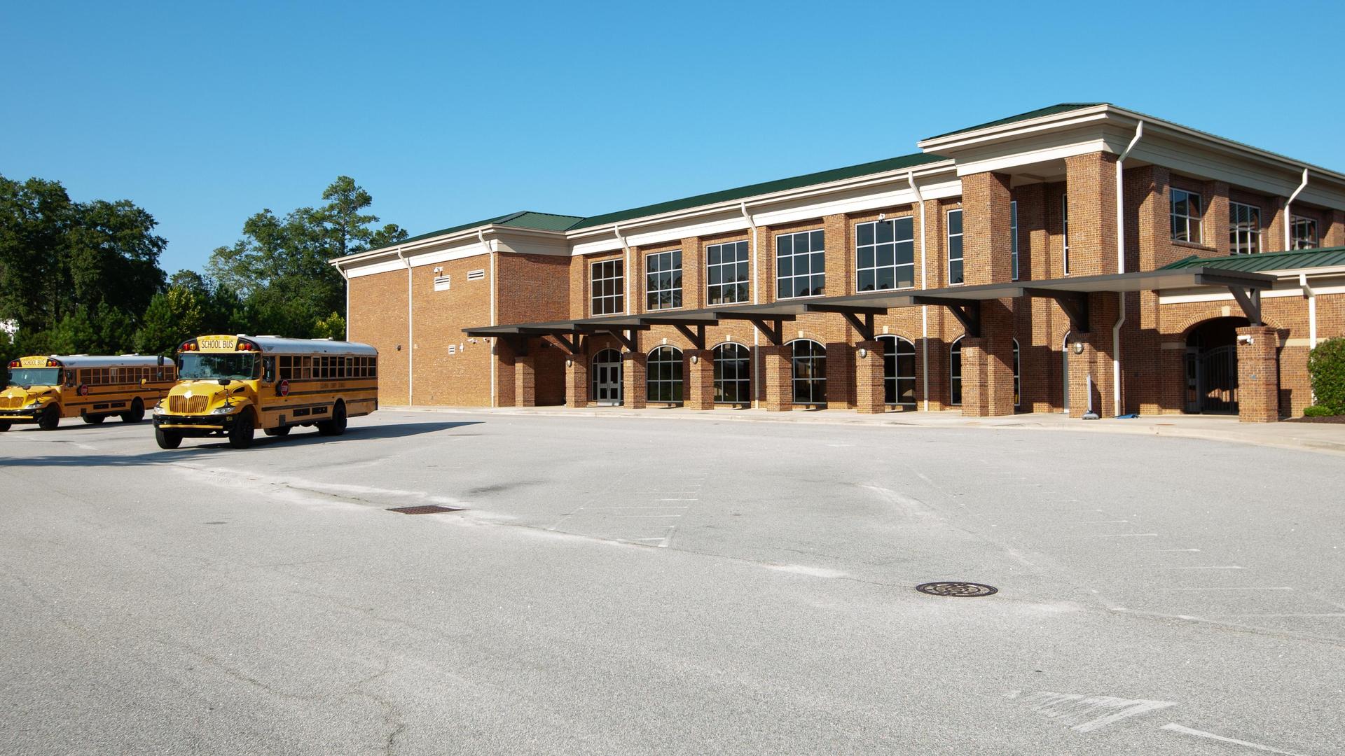 Yellow school buses parked in front of a modern brick school building.