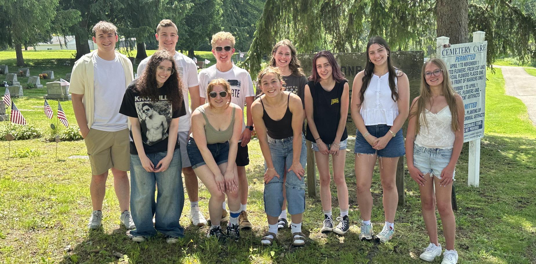 Group of teenagers posing together outdoors, smiling in a green park setting.