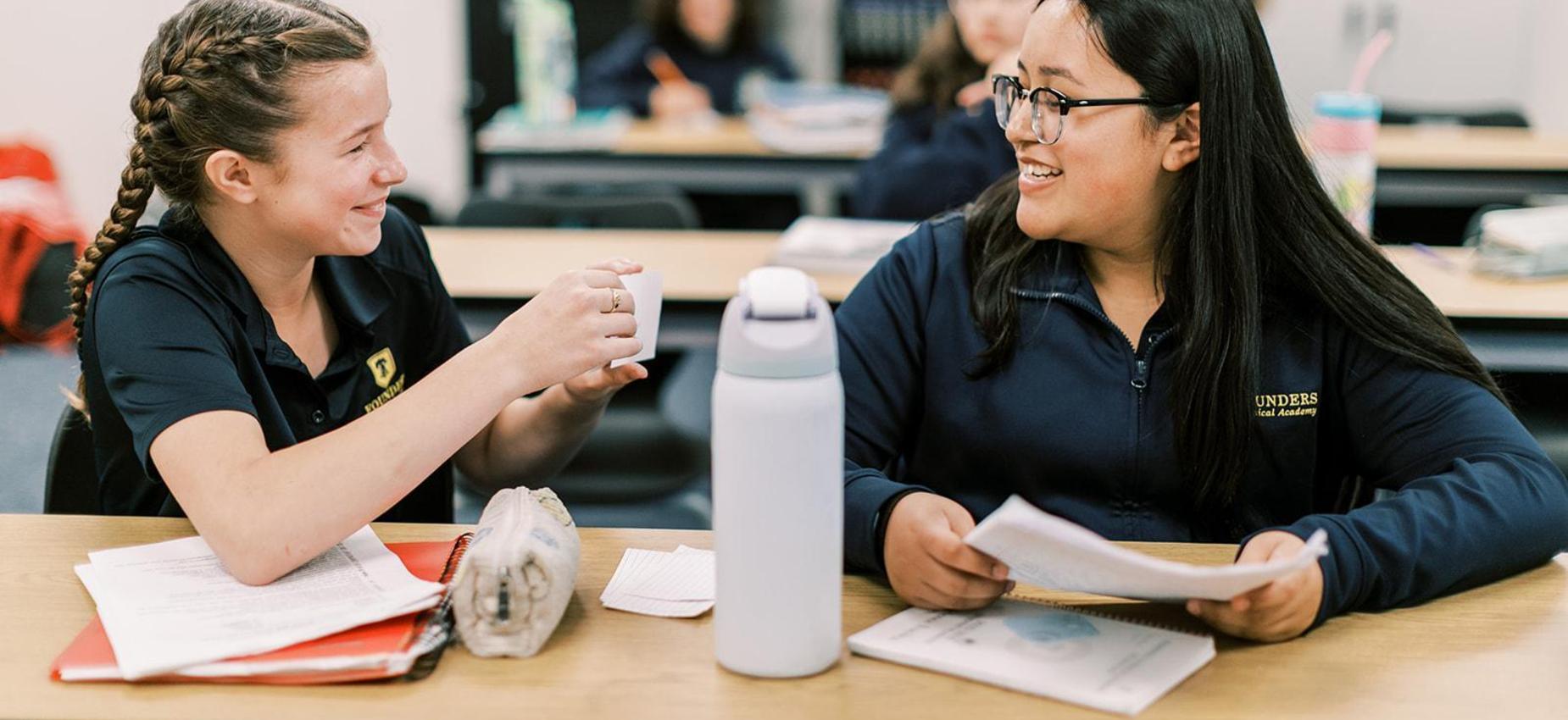 Two middle school students smile while studying together at a desk