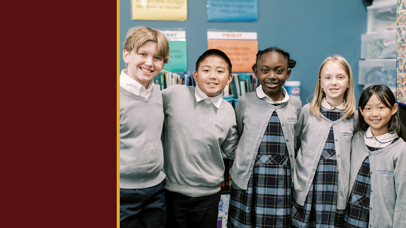 Four smiling students in gray sweaters stand together in a classroom