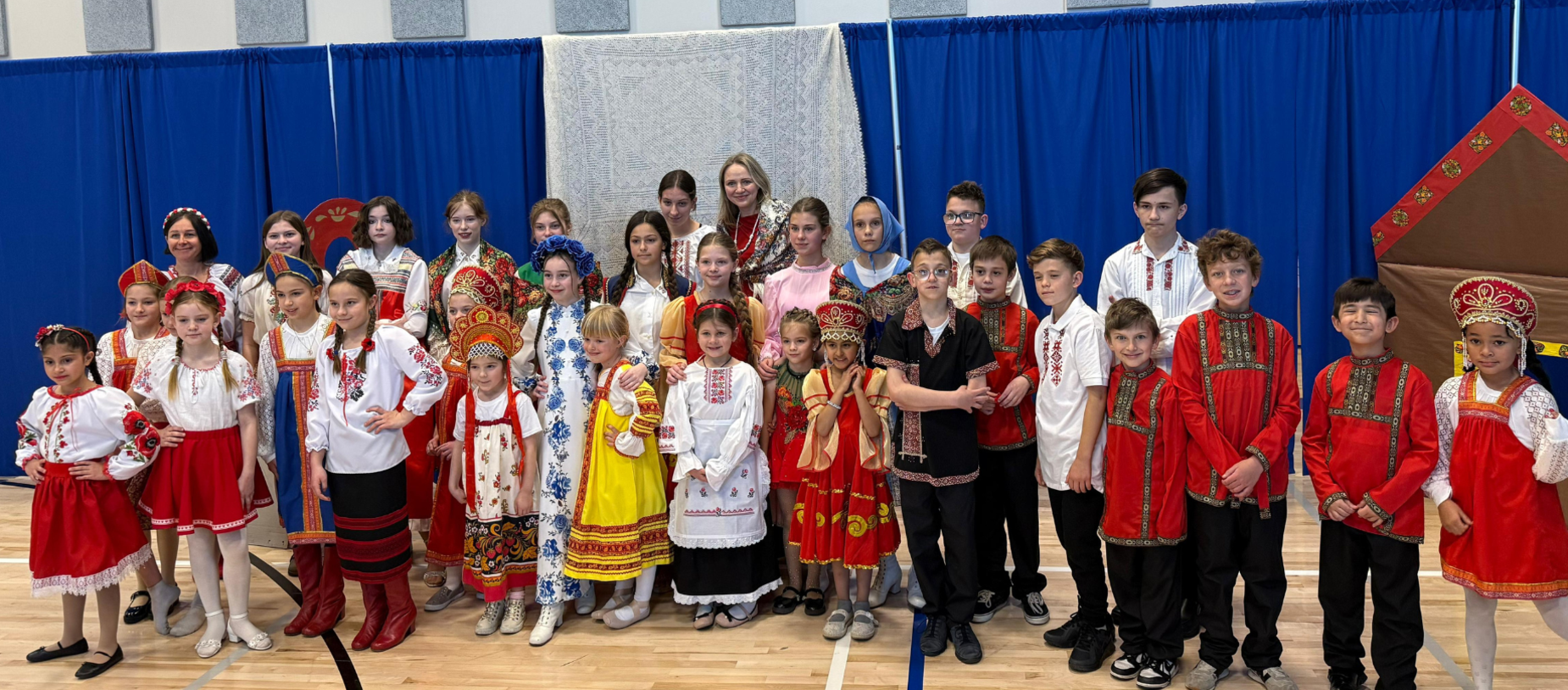 Group of children and adults in traditional costumes, standing together in a hall.