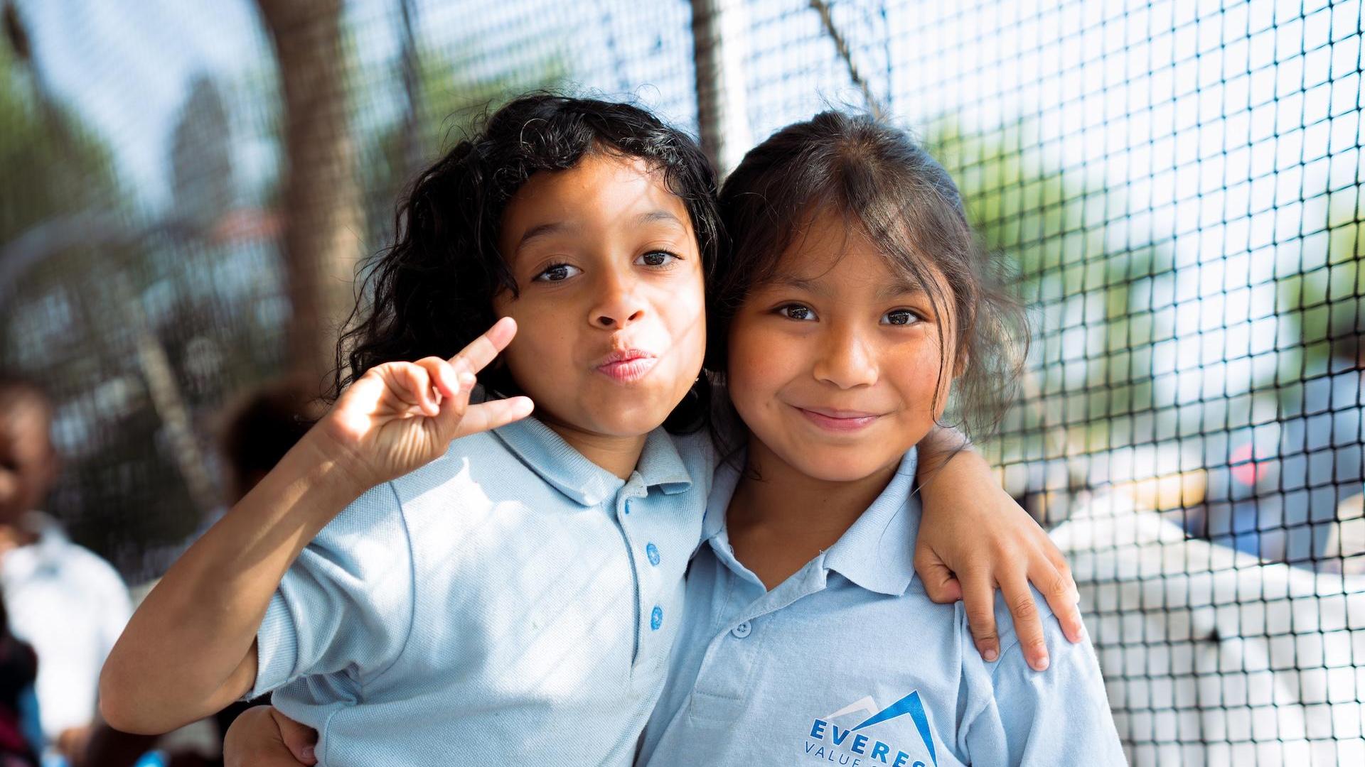 Two girls posing together with smiles, one making a peace sign.