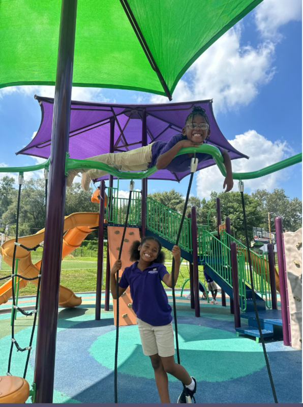 Two scholars climb on the playground and smile