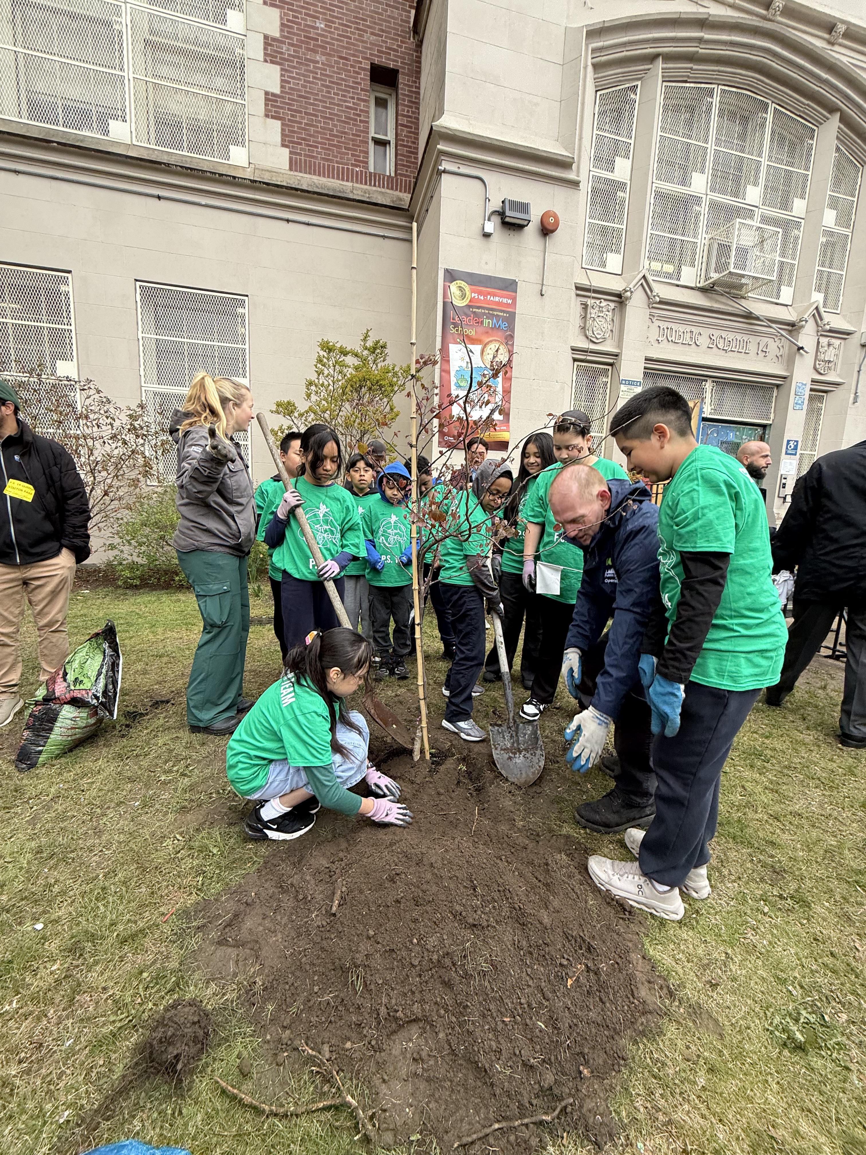 green team students wearing green tshirts with doe officials planting a tree