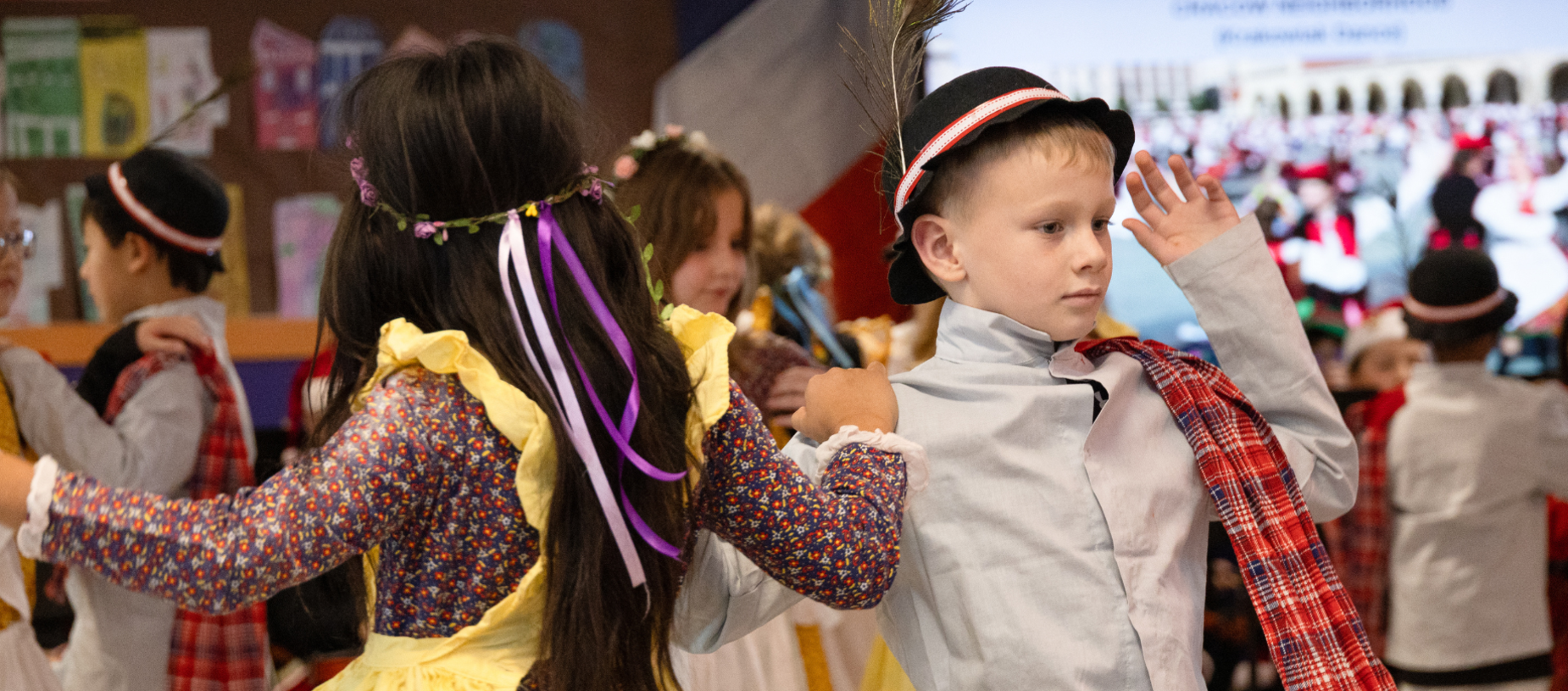 Children in traditional costumes dance together at a school event.