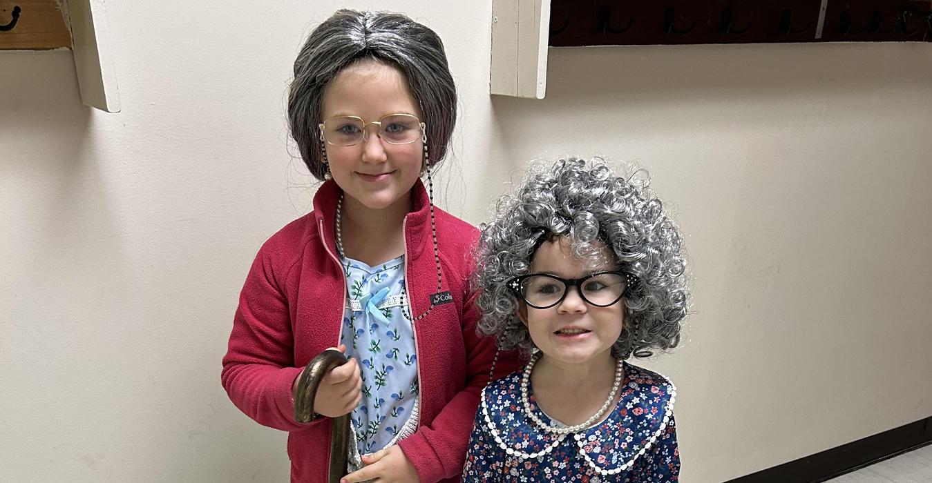 Two children dressed in costumes; one as an old lady with gray hair and a cane.