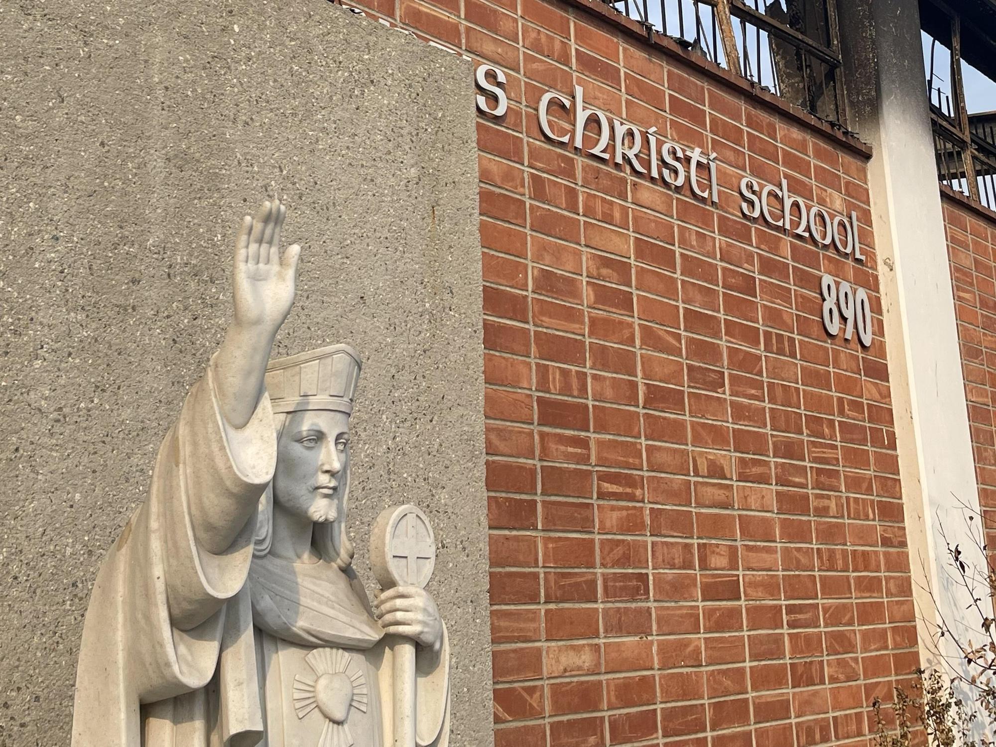 Statue and brick sign of a school with the name and number displayed.