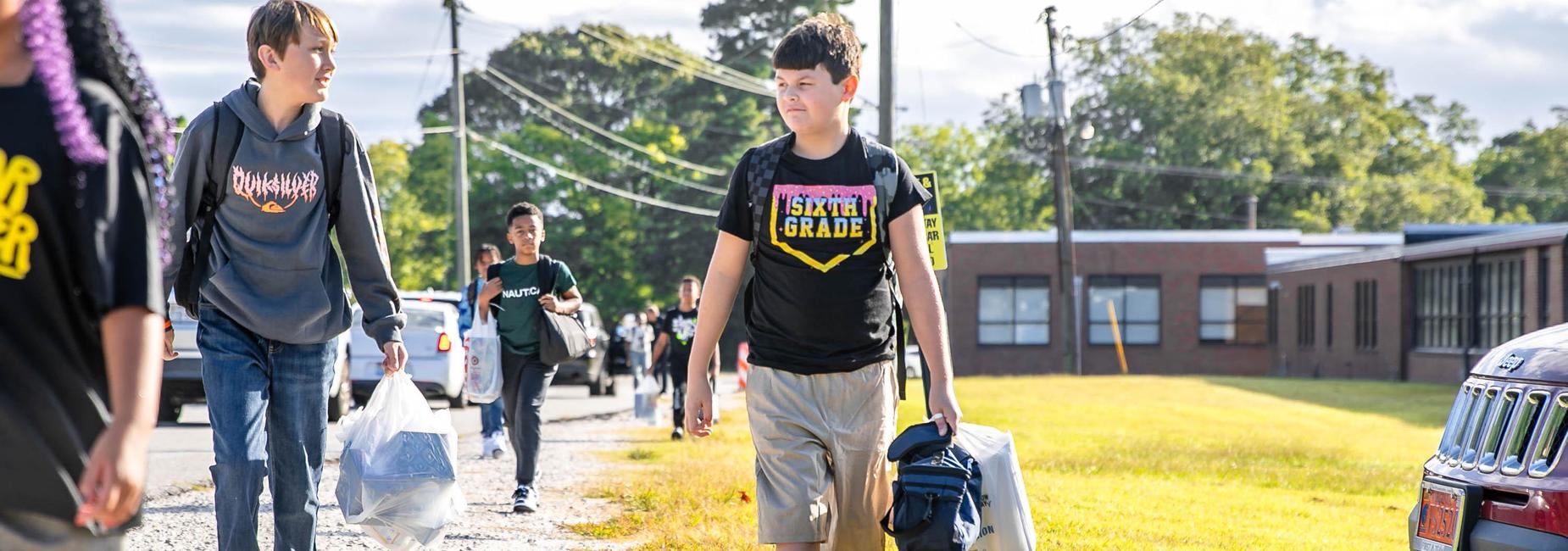 Students walking on a sidewalk towards a school, chatting and carrying backpacks.