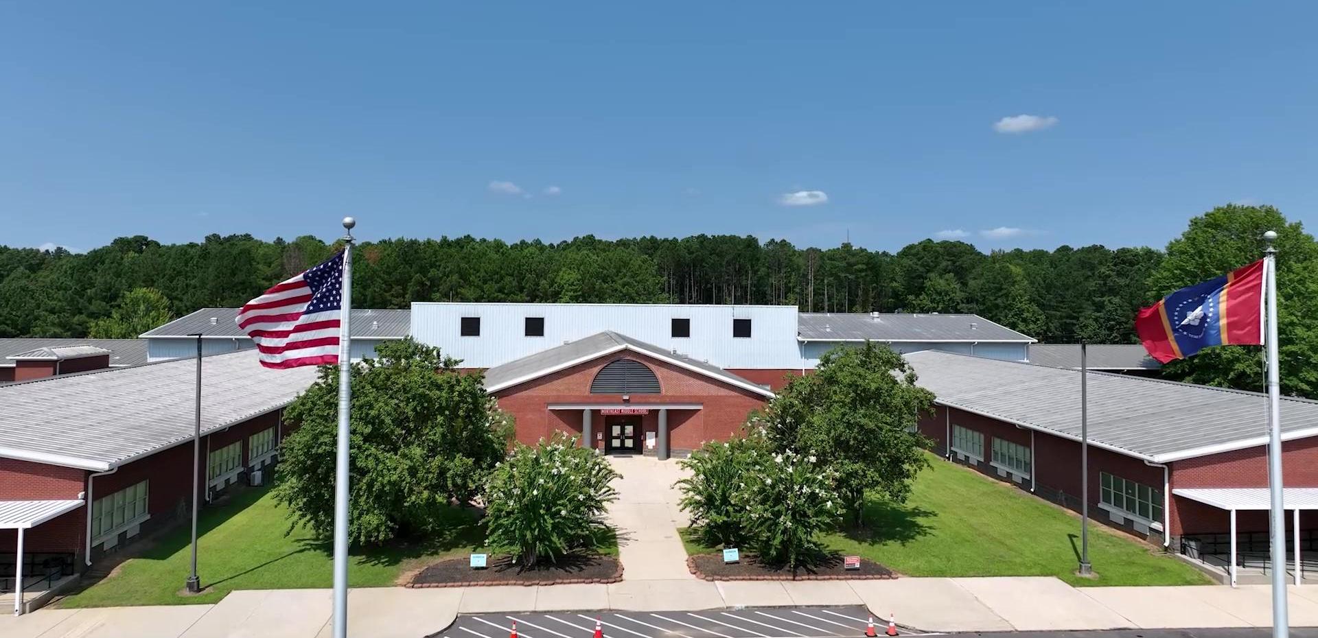 Red brick school building with flags and green lawn under a blue sky.