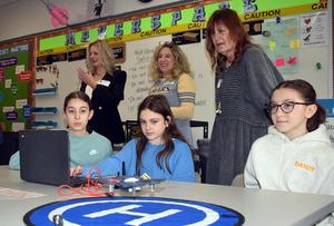 Three adults watching three students using a laptop to fly a drone.