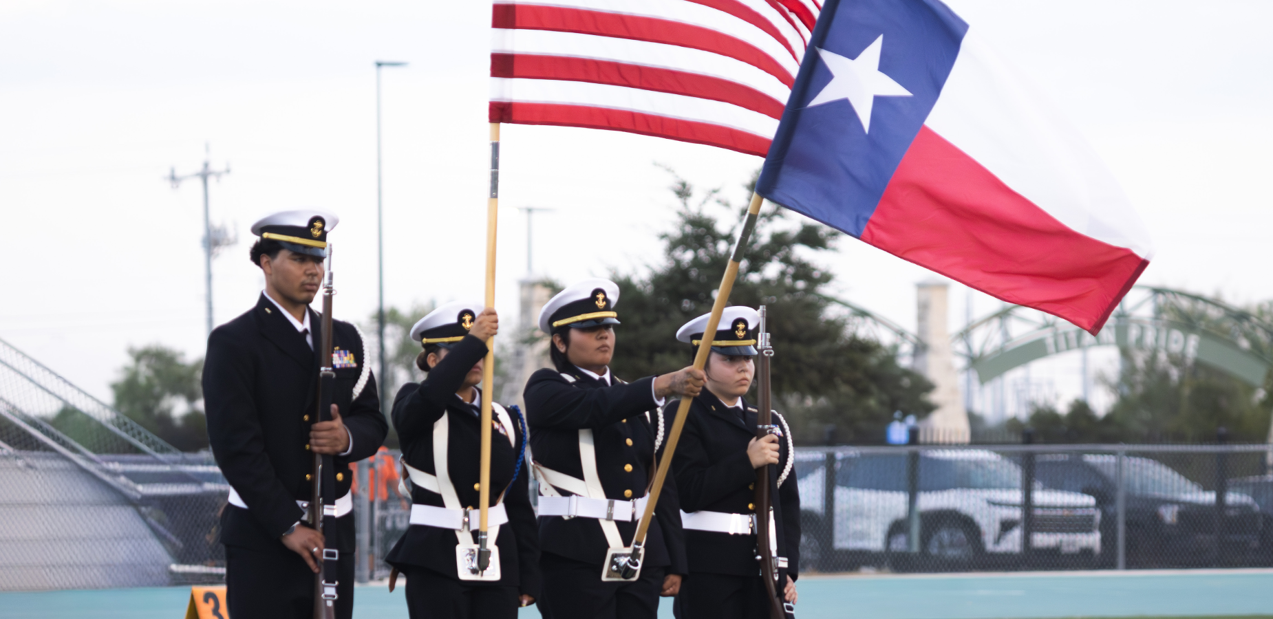 Four uniformed individuals hold a Texas flag and an American flag during a ceremony.