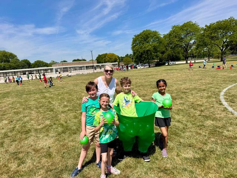 Group of children holding green balls with an adult in a grassy outdoor setting.